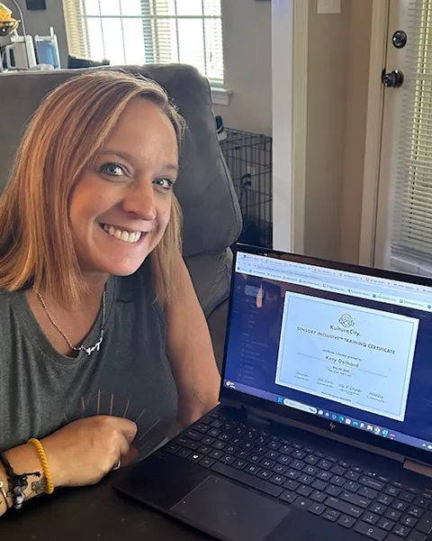 Katy Dothard at a laptop showing a KultureCity certificate